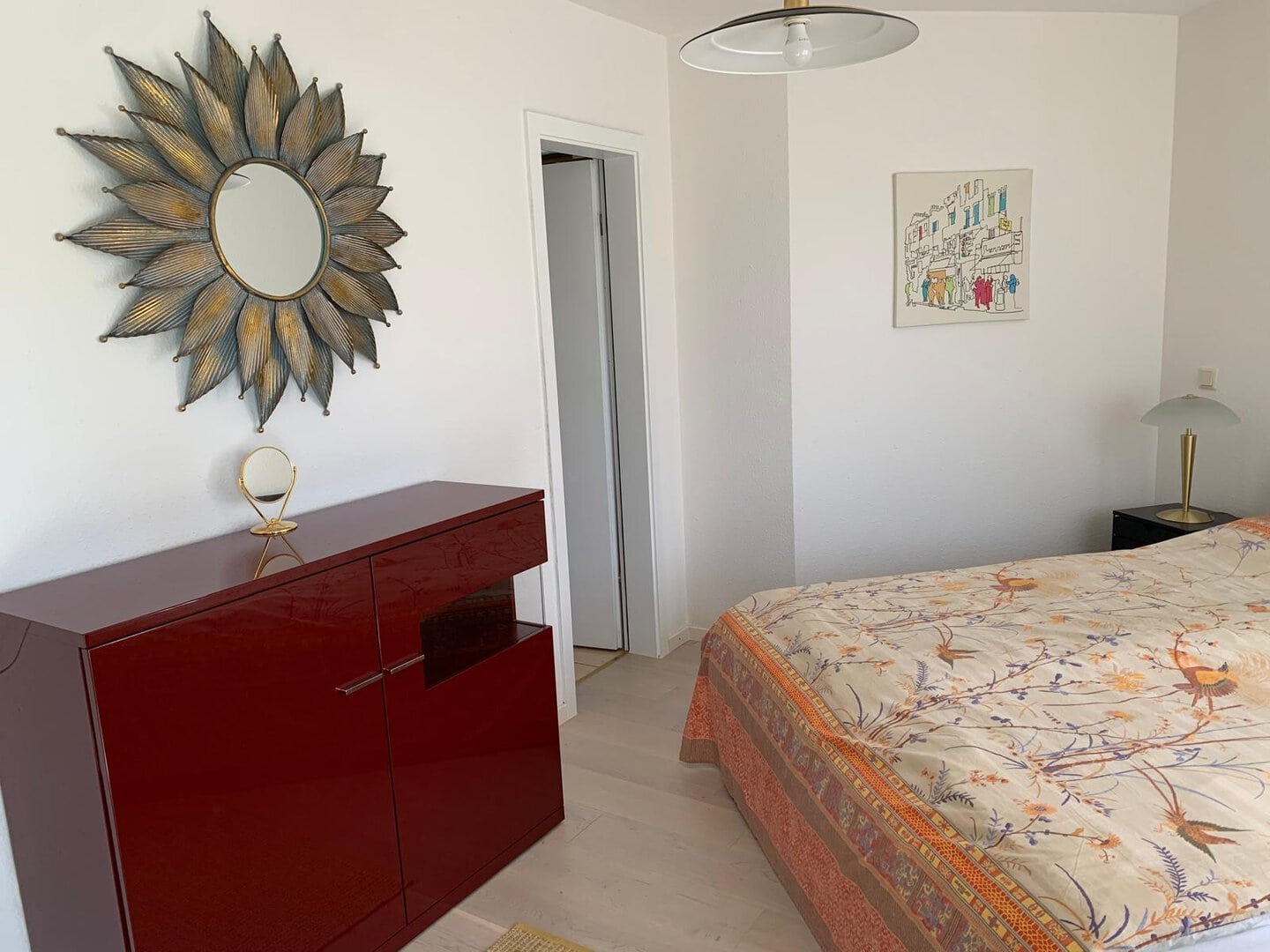 Modernes Schlafzimmer mit rotem Sideboard, Wanddeko und komfortablem Bett.